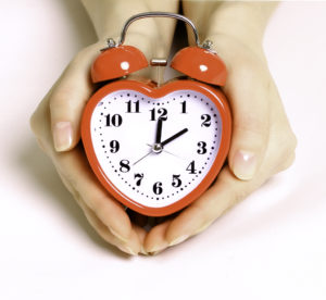 person cupping red heart-shaped alarm clock in hands