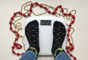 top view of female feet wearing Christmas tree socks standing on weight scale that reads 2022