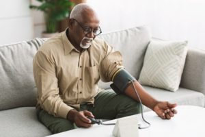 Senior African American Male Sitting On Couch At Home Measuring His Blood Pressure