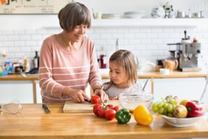 Senior woman and little girl chopping vegetables in the kitchen at home