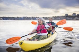Older adult couple kayaking on a lake on partly cloudy day