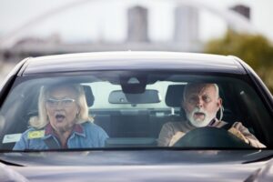 Shocked senior couple about to crash in a car. The view is through windshield.