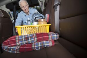 LV Senior man prepares for roadside emergency with survival items in his truck.  As severe winter weather hits, this man loads a basket of survival items and a warm blanket into the back of his truck.