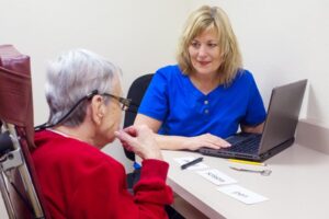 Blond Caucasian speech language pathologist treats communication skills of a senior aged woman in a clinic setting. Visual comprehension addressed. Patient matches objects to a field of three single written words.